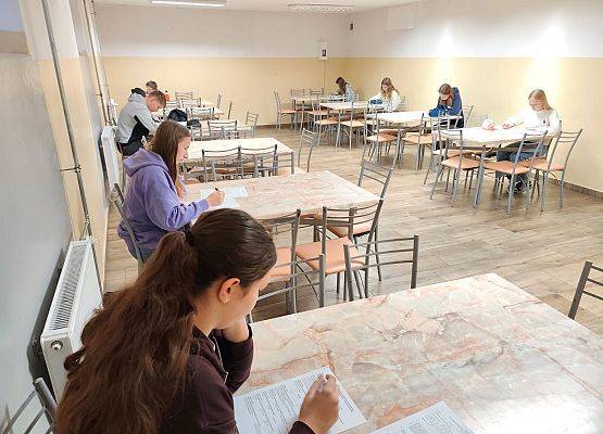 Uczestnicy konkursu ze Szkoły Podstawowej w Kłodawie (fot. J. Krawczykiewicz) Widok na salę. Przy kilku stolikach siedzą uczniowie i rozwiązują test na kartach odpowiedzi.
