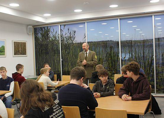 Etap gminny konkursu Poznajemy Parki Krajobrazowe Polski Uczestnicy konkursu siedzą przy stolikach, z przodu sali kierownik ZPK w mundurze witający konkursowiczów.