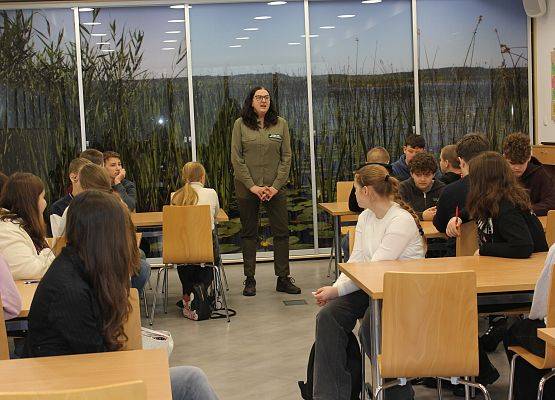 Etap gminny konkursu Poznajemy Parki Krajobrazowe Polski Uczestnicy konkursu siedzą przy stolikach, z przodu sali Grażyna Jaszewska tłumacząca szczegóły konkursu.