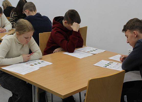 Konkursowicze w czasie rozwiązywania testu Uczestnicy siedzą przy stolikach, przed nimi karty do rozwiązywania testu konkursowego.