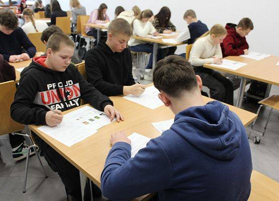 Konkursowicze w czasie rozwiązywania testu Uczestnicy siedzą przy stolikach, przed nimi karty do rozwiązywania testu konkursowego.