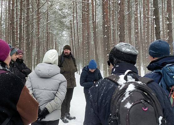Grupa ludzi ubranych w sportowe zimowe stroje, z przodu przewodnik prowadzący spacer.